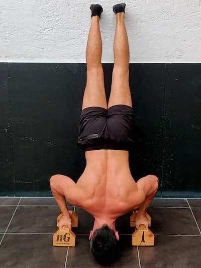 Assisted handstand push-up facing the wall with extended range